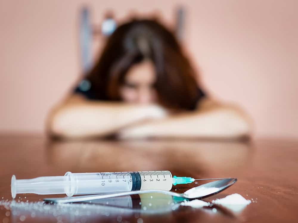 woman looks into heroin on a spoon and syringe during while struggling with addiction withdrawal
