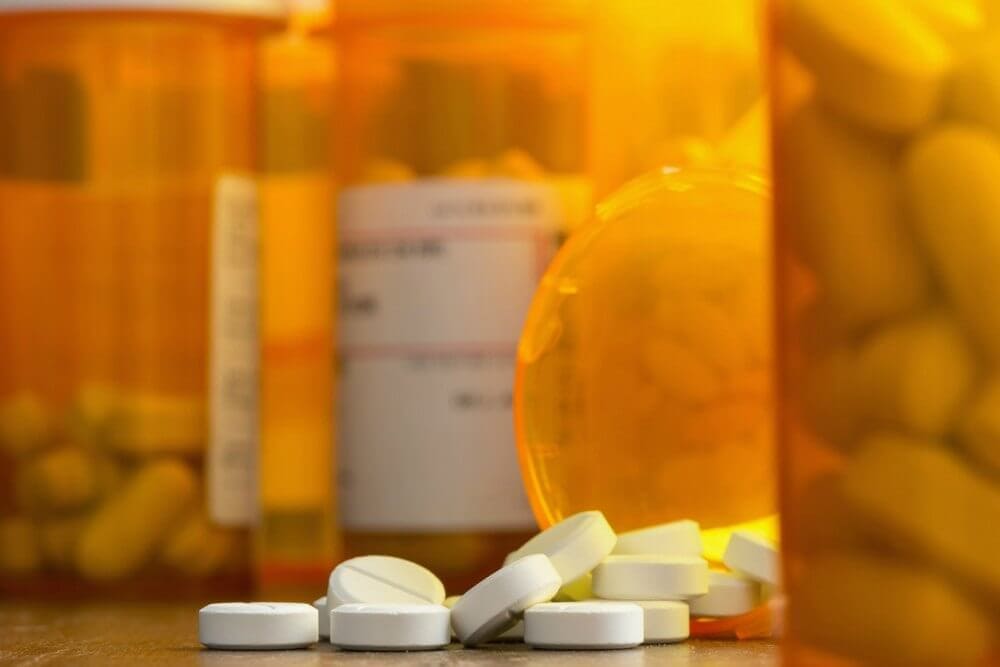 white percocet pills scattered on a table with orange pill containers behind 