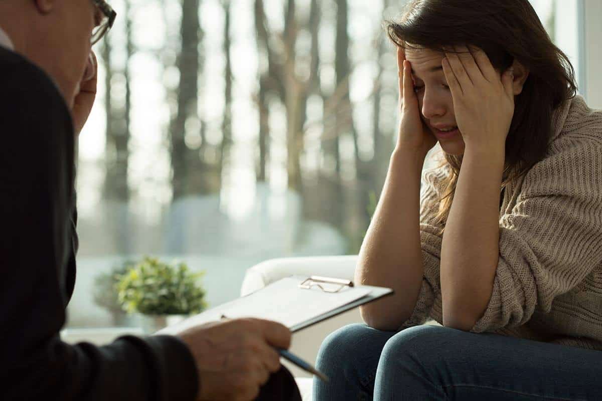 a distressed woman holds her temples while talking to a therapist