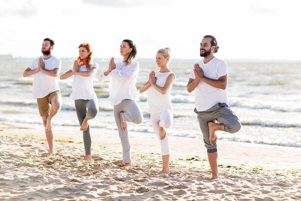 lighthousetreatment-7-ways-to-alleviate-anxiety-without-drugs-article-photo-yoga-fitness-sport-and-healthy-lifestyle-concept-group-of-people-in-tree-pose-on-beach-519449413