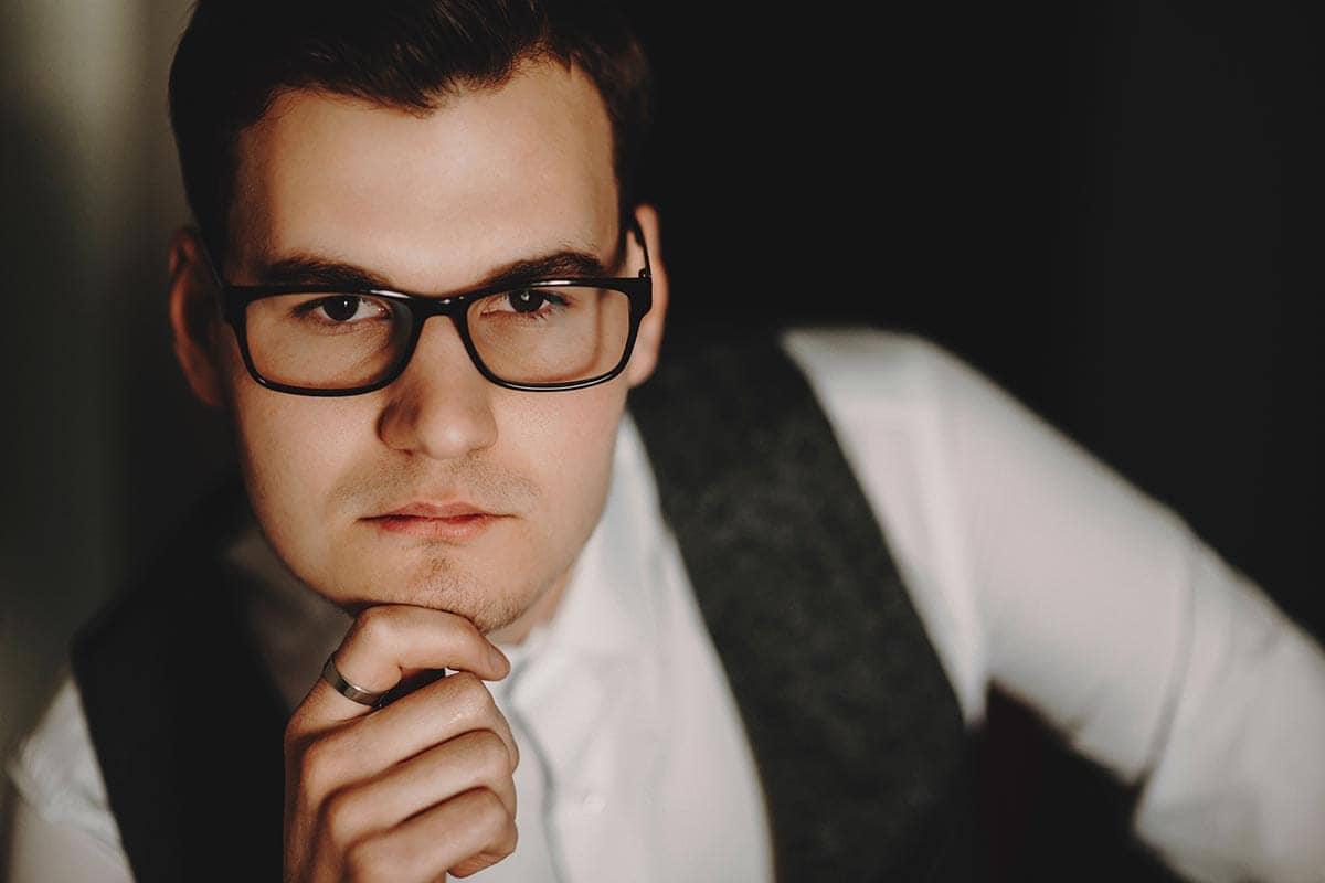 a man wearing glasses holds his chin with his hand appears to be thinking hard