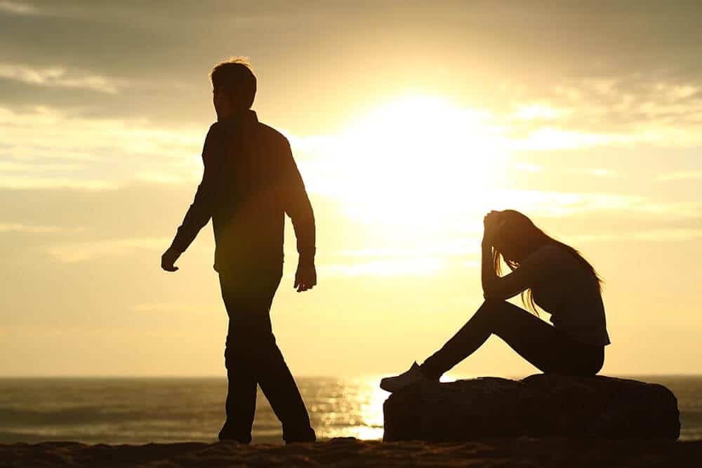 silhouette of a couple with the man walking away from the woman sitting by the beach