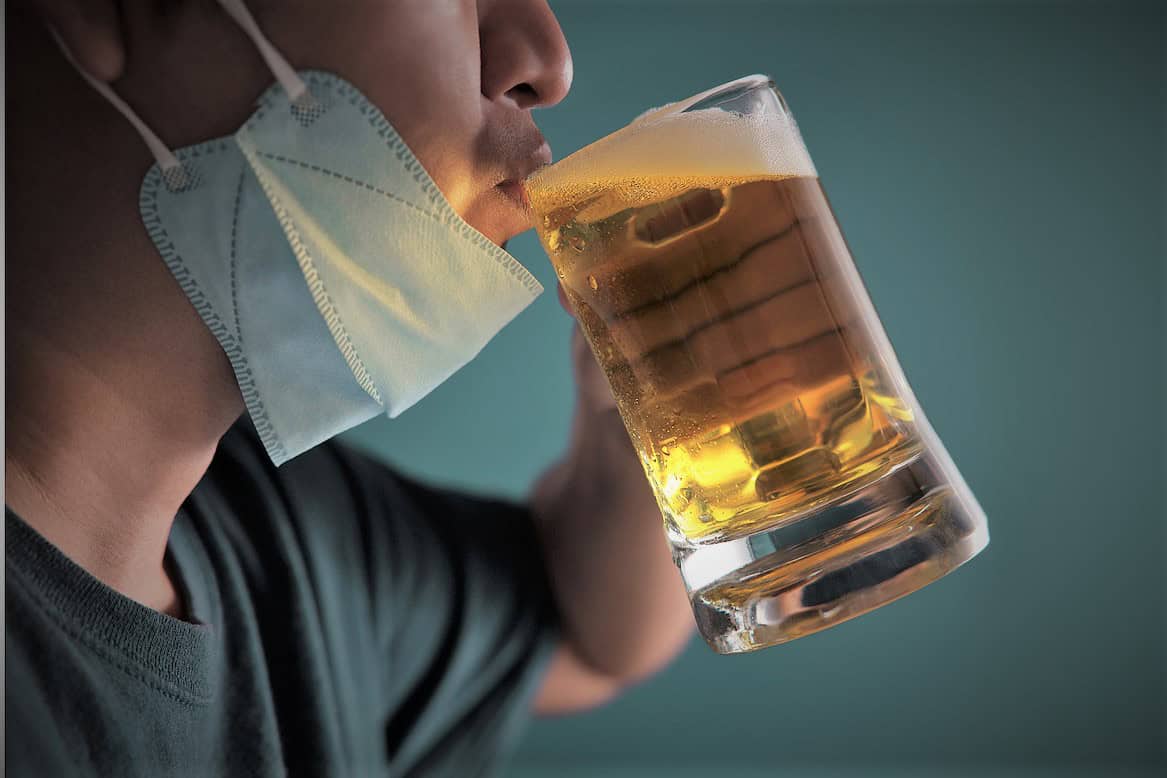 a man with his face mask down drinking a pint of cold beer 
