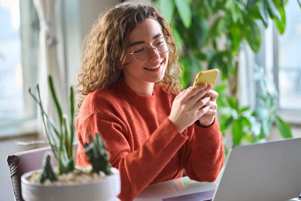 A woman in orange shirt reading happy Thanksgiving messages with green plants in the background