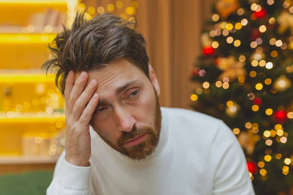 A man with a hangover with a Christmas tree in the background 