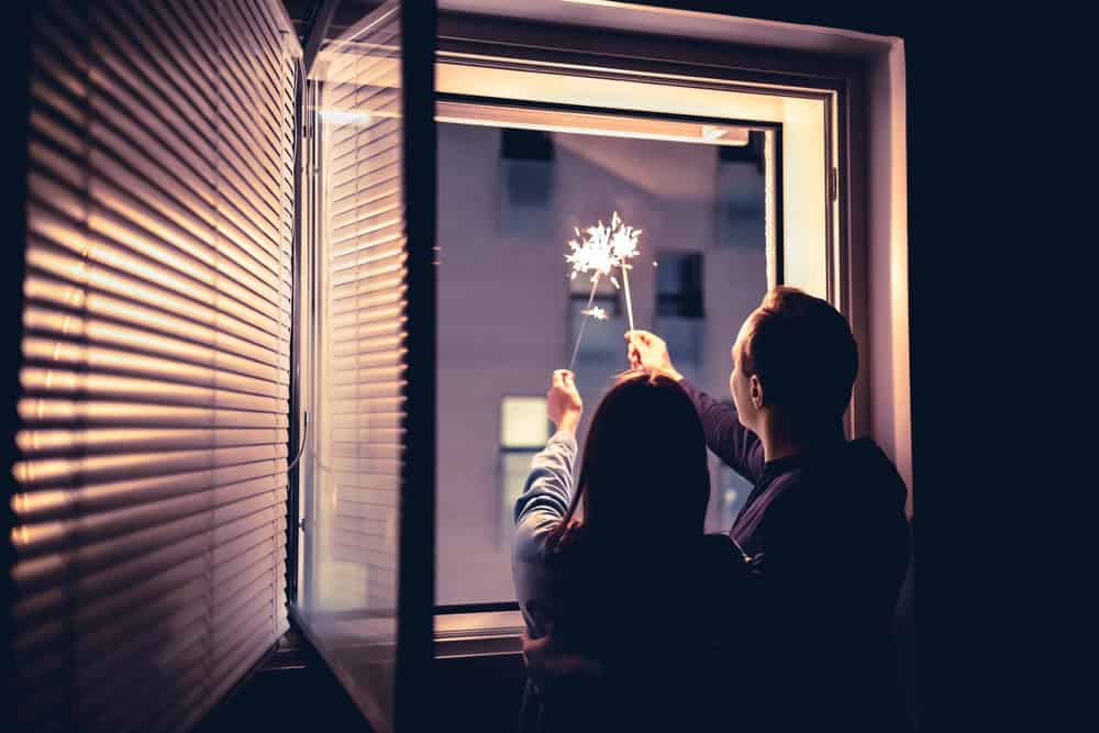 A couple’s silhouette in front of the open window, holding sparklers to celebrate the New Year