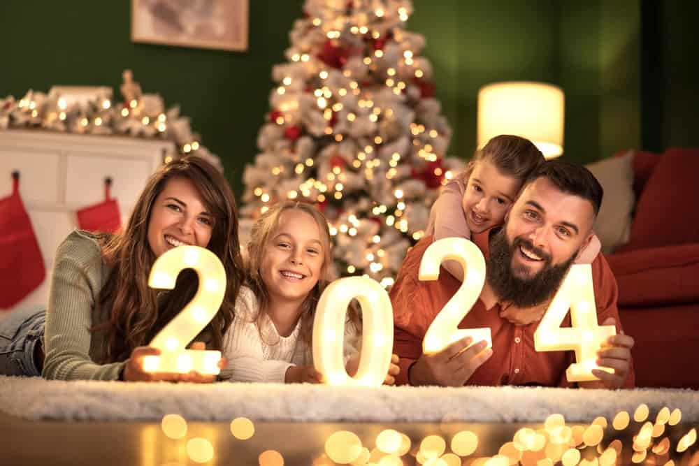 A young family on the couch in front of the Christmas tree, holding the numbers to form year 2024