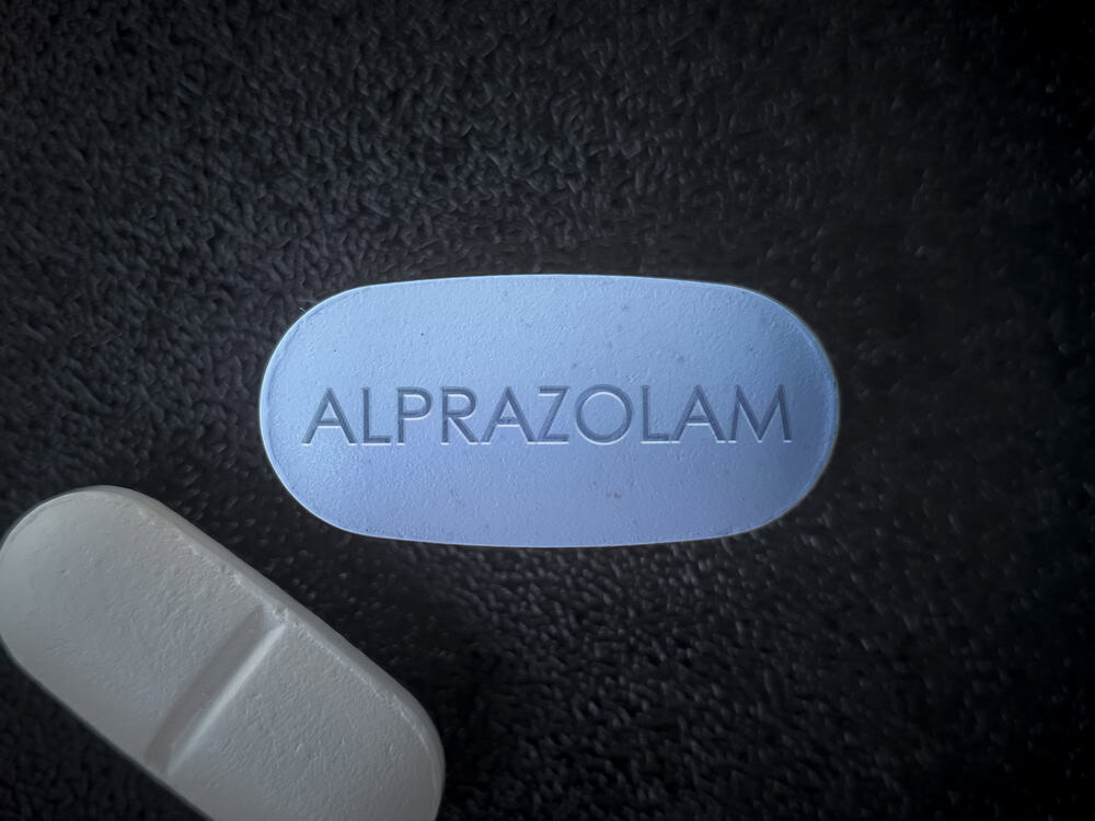 Blue alprazolam bar with an imprint and a white plain tablet on a black background