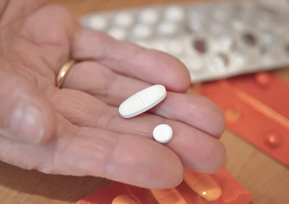 A hand with gold ring handling two white drug pills.