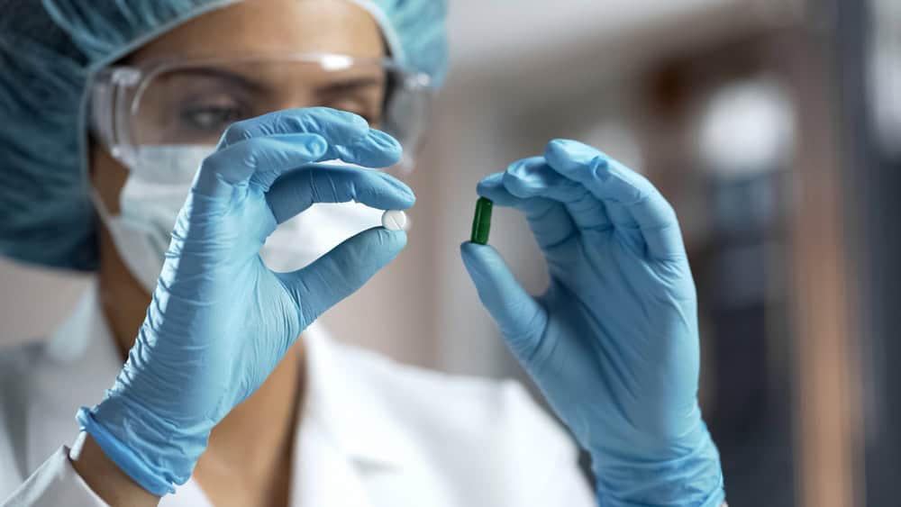 A pharmacology expert comparing two pills while wearing blue gloves.