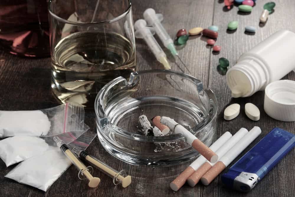Glass of alcohol with different drugs and paraphernalia on a wooden table