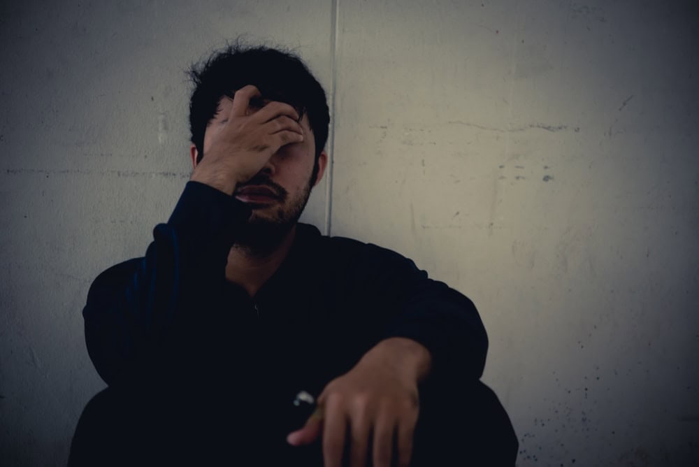 Man addicted to meth and crack sitting on the floor covering his face 
