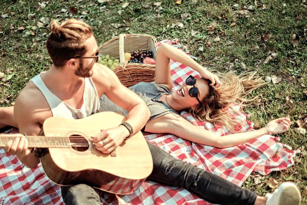 Couple having a Valentine’s Day picnic with the man serenading the woman