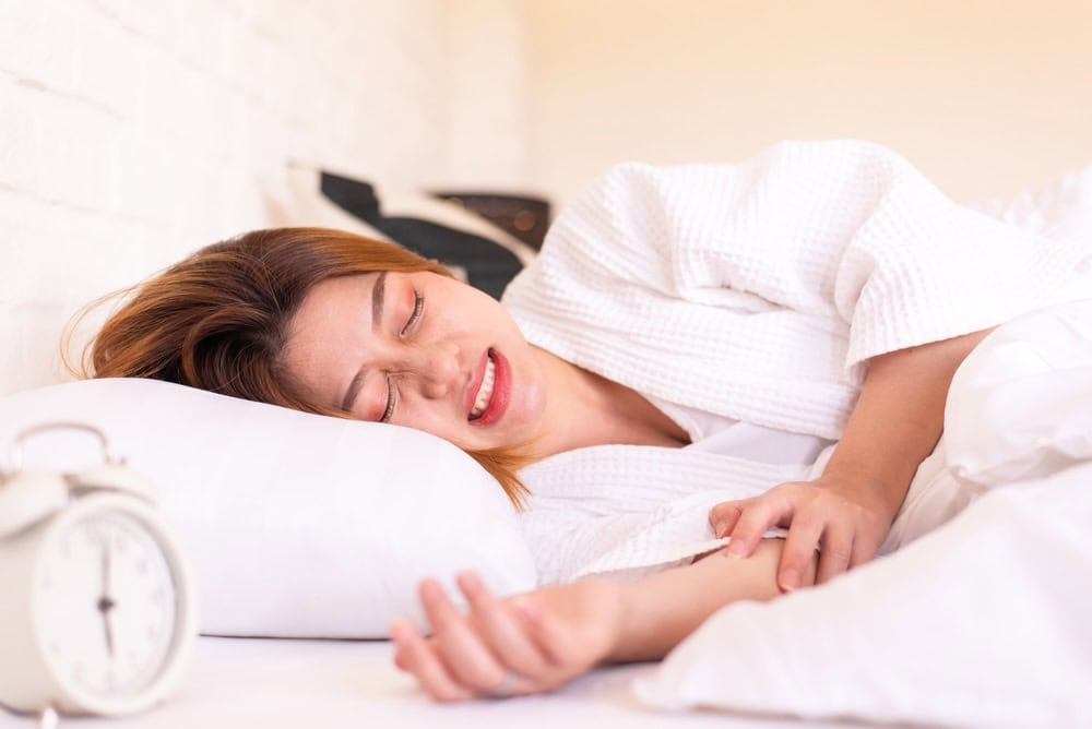 Woman sleeping in bed, grinding her teeth resulting in coke jaw