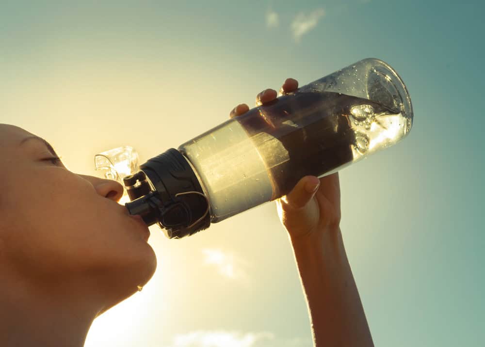Woman drinking from a green bottle of water to detox