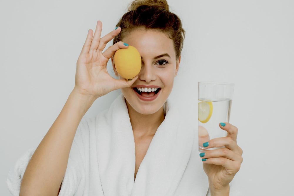 Woman holding a lemon and a glass of lemon-infused water 