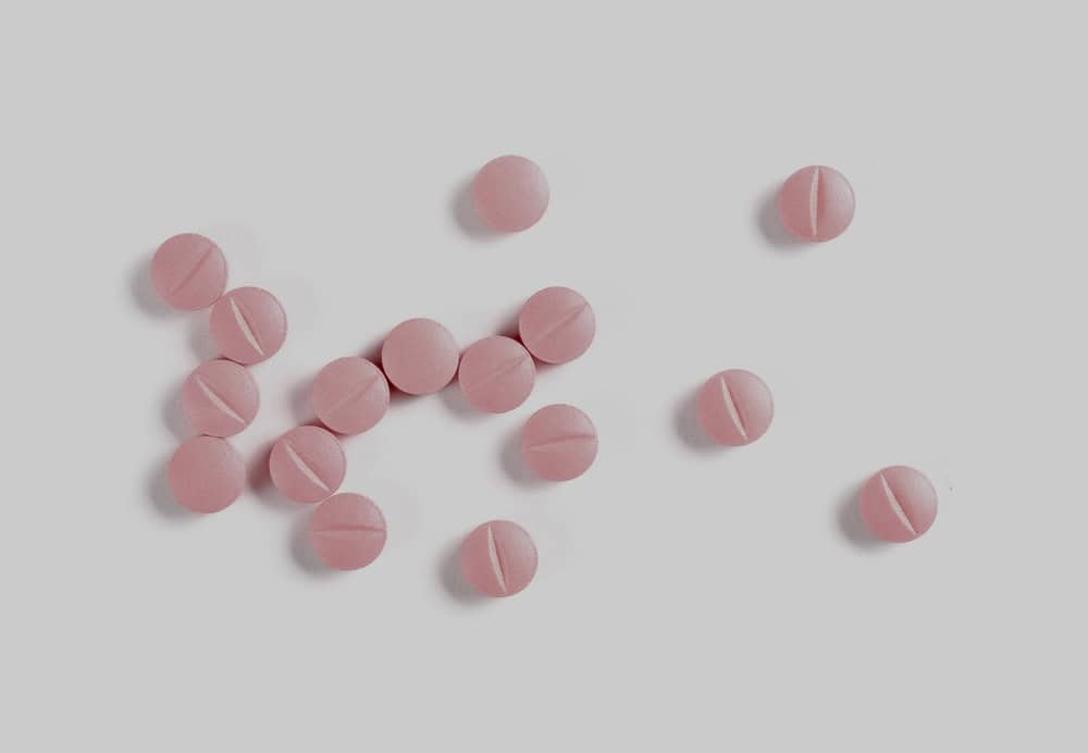 Pink pills scattered on a white surface
