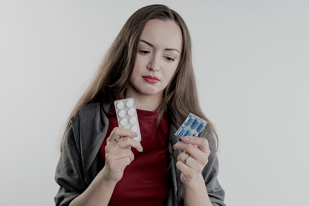 Woman holding to packets of medicines in her hands with a confused look on her face