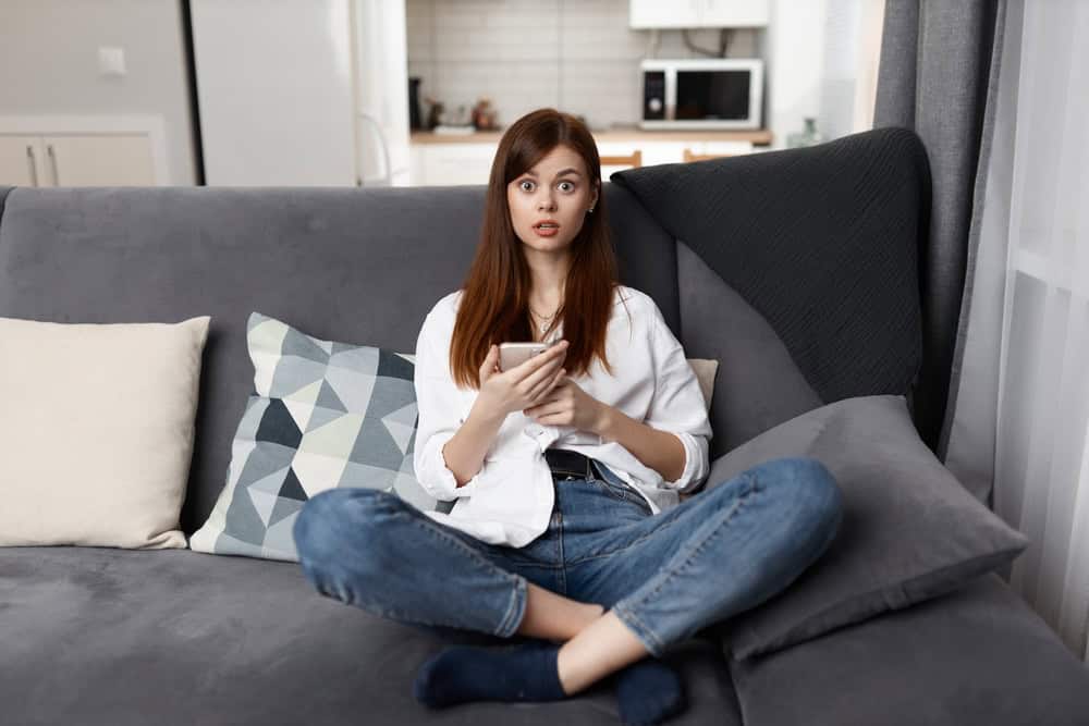 Woman sitting on a couch with a phone, surprised look on her face