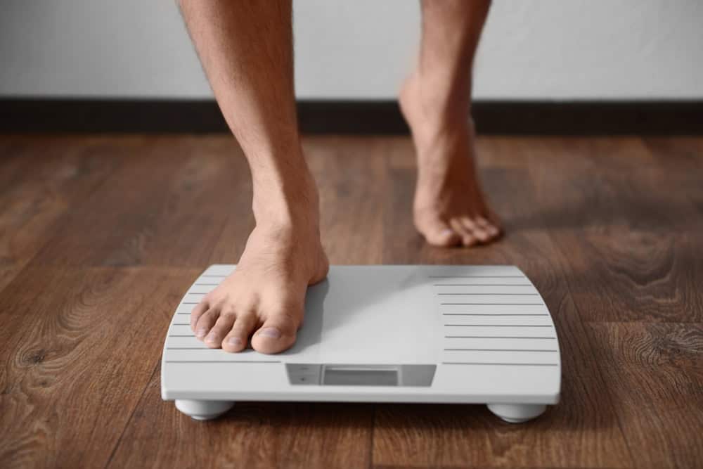 Legs of a man stepping on a weighing scale