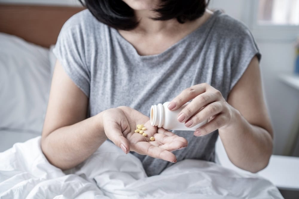 Female in bed pouring Trazodone pills on her hand