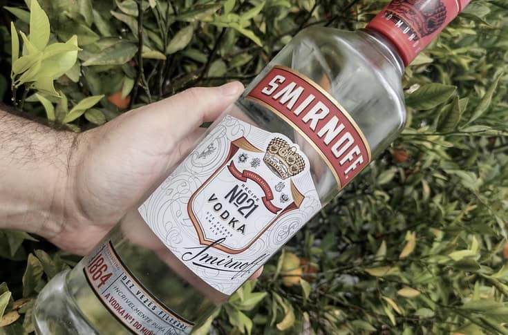 Hand holding a bottle of vodka with leaves in the background 