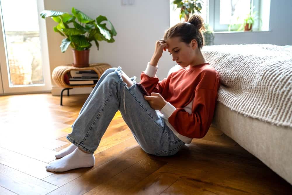 Teen sitting by her bed looking at her social media feed on her phone
