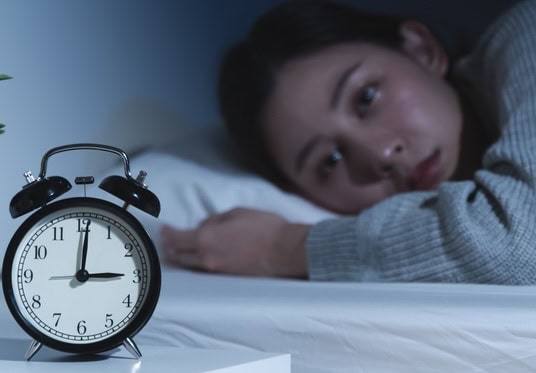 Woman lies awake in bed looking at the bedside clock