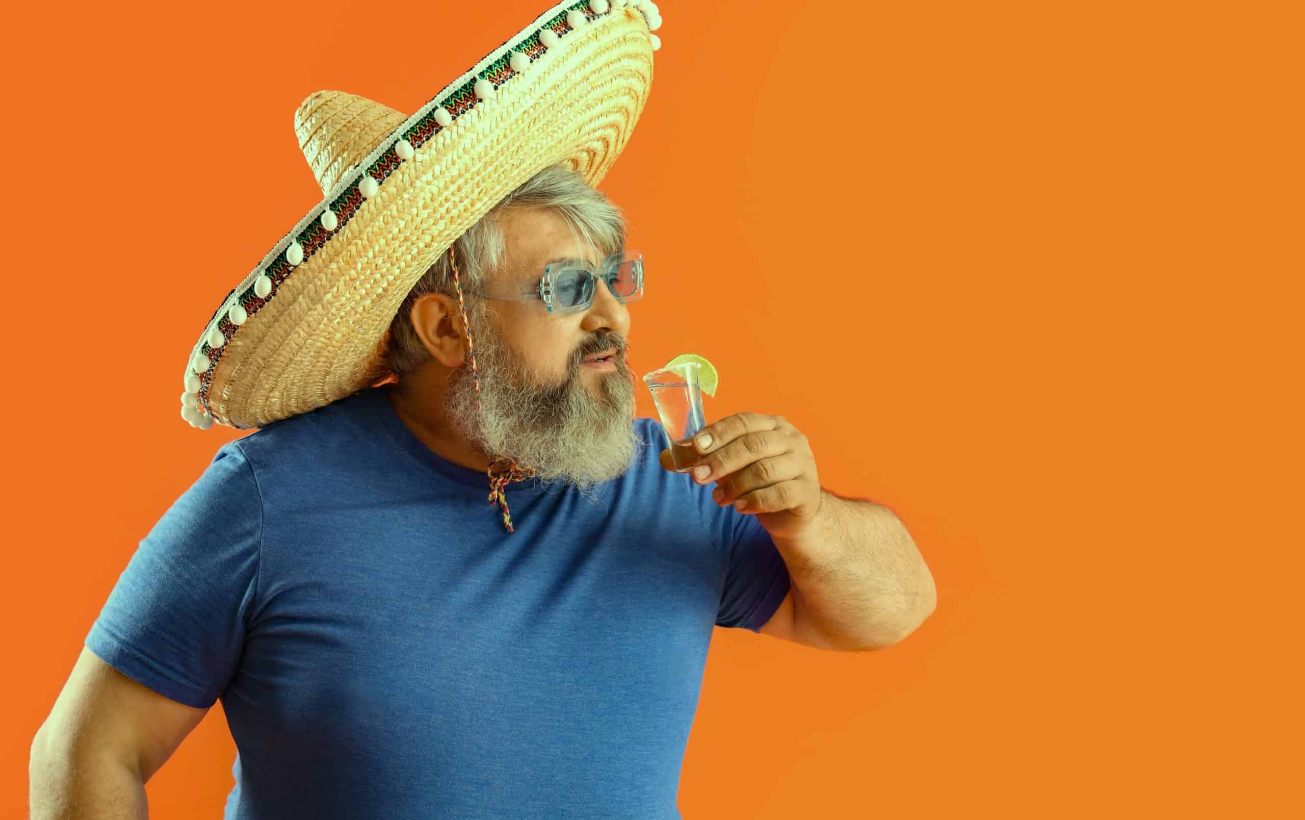 An old man with a Mexican hat drinking a shot of tequila