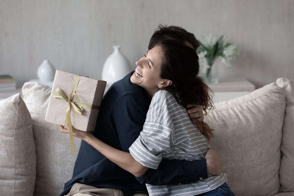 Woman congratulating her husband on sobriety anniversary holding a gift
