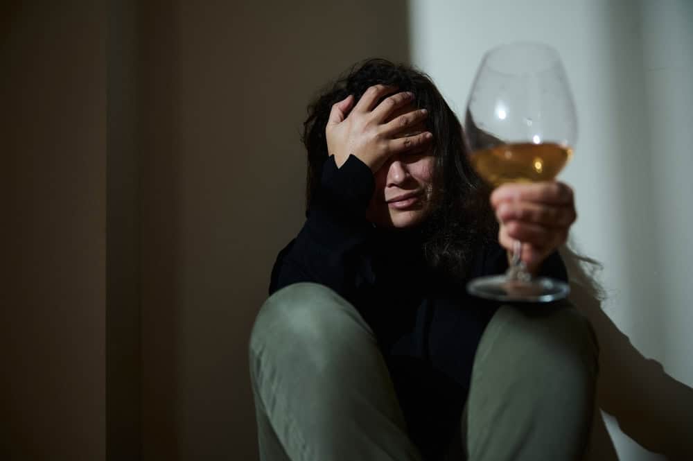 Depressed woman crying holding a glass of wine needing help