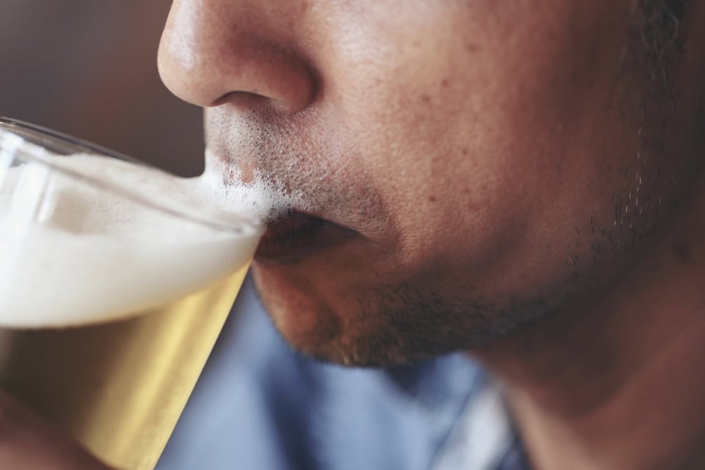 Closeup of man drinking beer with foam binge drinking 