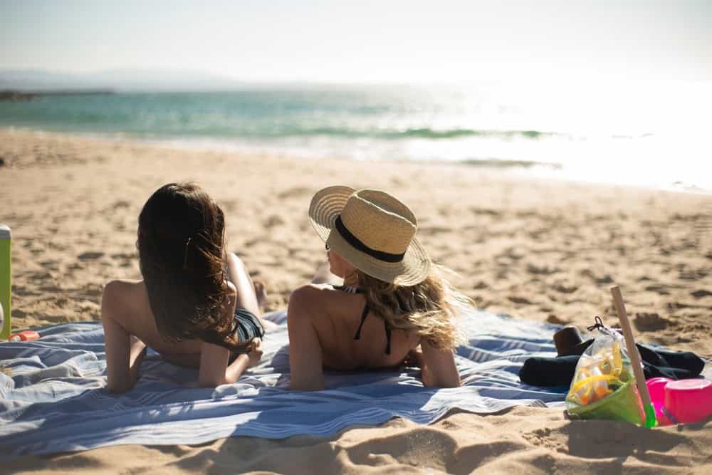 Two women lounging on the beach while on vacation to avoid triggers for addiction relapse