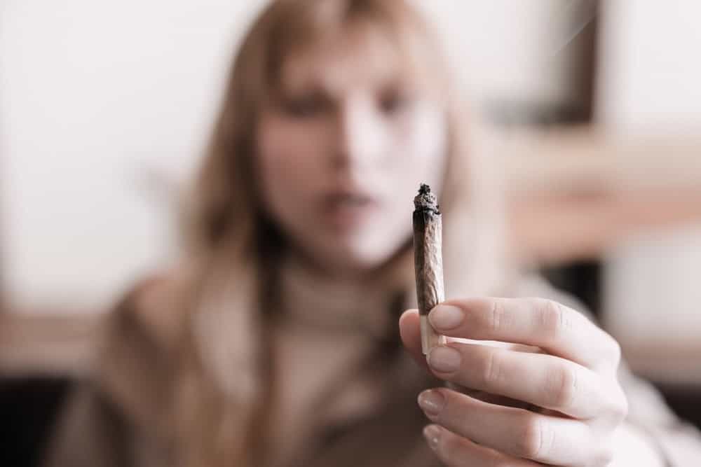 Adult female holding up a weed joint thinking about the benefits of giving up weed 