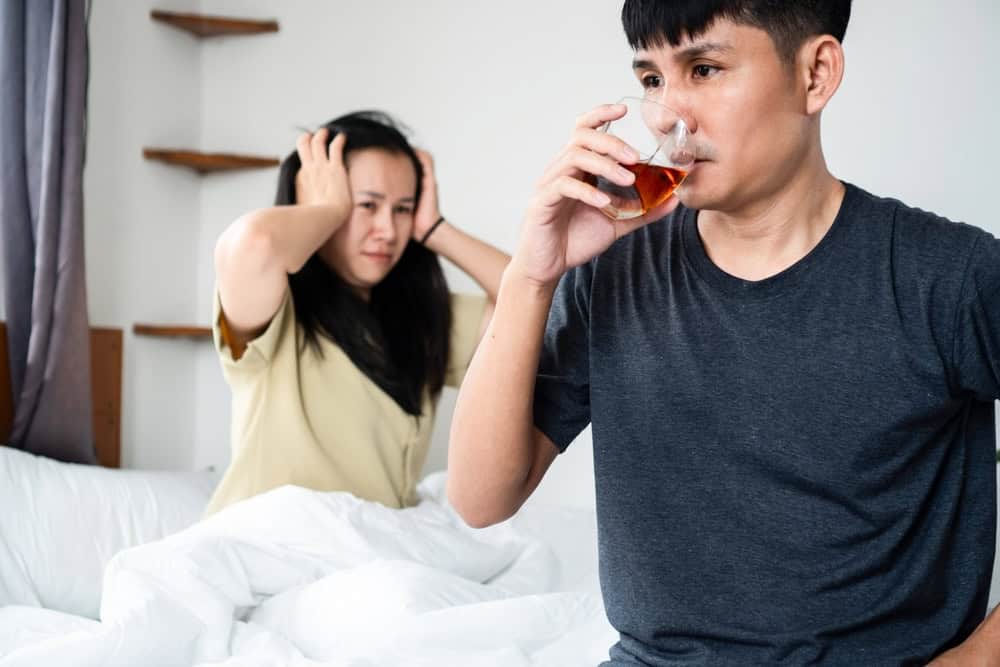 Frustrated woman seeing her partner drinking alcohol in bed