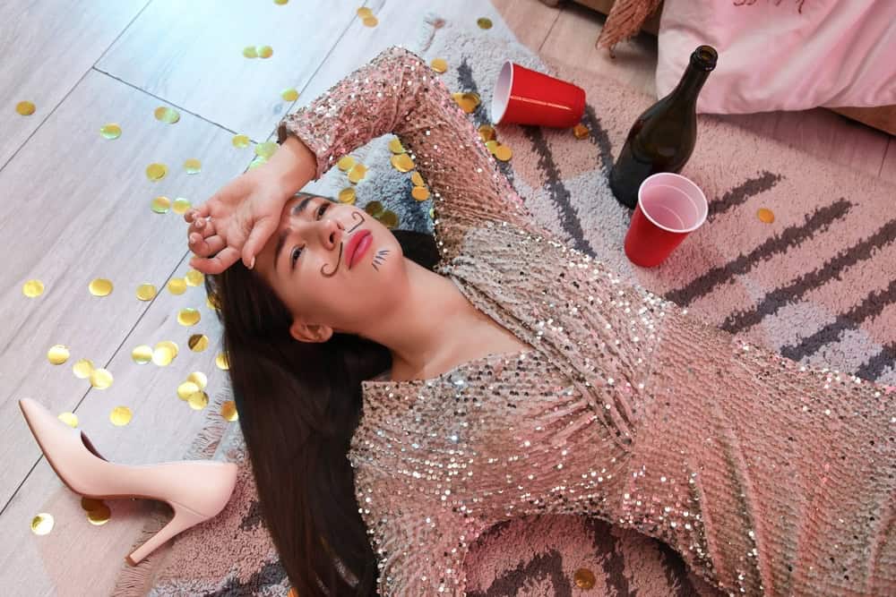 Drunk woman on the floor after a party wondering if alcohol makes her face puffy